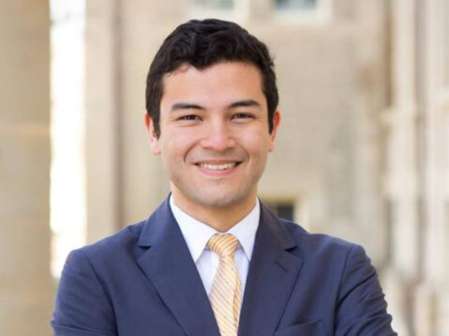 Peter Carrera wears a suit and smile at the camera with his arms crossed